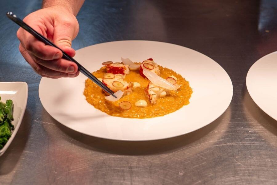 Behind the scenes at Blas Restaurant, chefs prepare a lobster risotto dish, combining fresh seafood with seasonal ingredients for the 2026 Summer Menu.