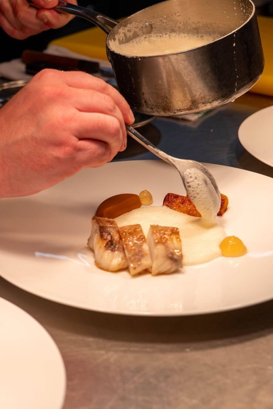 A chef at Blas Restaurant prepares fresh monkfish in the kitchen, showcasing carefully sourced seafood featured on the 2026 Summer Menu.