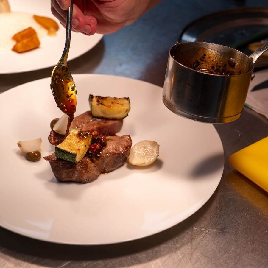 Behind the scenes in the Blas Restaurant kitchen, chefs prepare tender pork collar as part of the 2026 Summer Menu, showcasing locally inspired seasonal cooking.